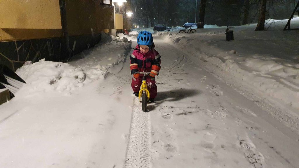 LapsI Aajaa potkupyörällä kerrostalon pihamaalla pimeänä talvi-iltana lumisen maiseman ympäröimänä..